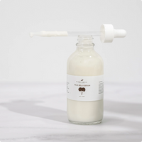 A clear glass bottle filled with white serum labeled True Belly Serum stands on a light surface. The dropper lid rests on top, with some serum visible on the dropper wand.